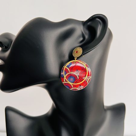 Boucles d'oreilles rondes en tissu wax rouge et bleu avec métal doré, affichées sur un présentoir en carton.