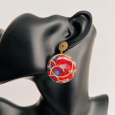 Boucles d'oreilles rondes en tissu wax rouge et bleu avec métal doré, affichées sur un présentoir en carton.