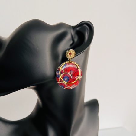 Boucles d'oreilles rondes en tissu wax rouge et bleu avec métal doré, affichées sur un présentoir en carton.