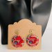 Boucles d'oreilles rondes en tissu wax rouge et bleu avec métal doré, affichées sur un présentoir en carton.