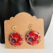 Boucles d'oreilles rondes en tissu wax rouge et bleu avec métal doré, affichées sur un présentoir en carton.